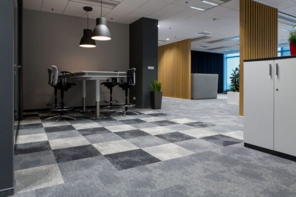 Wnętrze biura z drewnianymi lamelami na drugim planie i wykładziną w szachownicę w różnych odcieniach szarości
